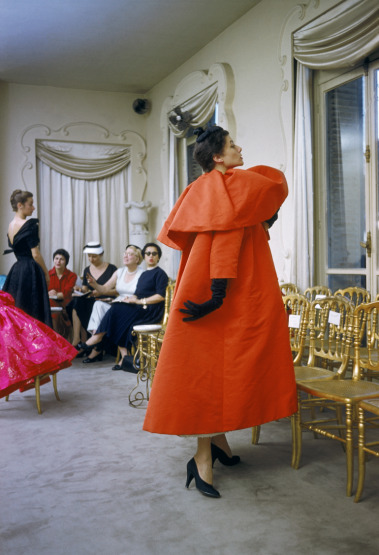 17-05/29/model-wearing-balenciaga-orange-coat-as-i-magnin-buyers-inspect-a-dinner-outfit-in-the-background-paris-france-1954-mark-shaw-mptvimagescom.jpg